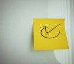 Yellow sticky note with a check mark symbol on a white background, ideal for reminders.