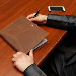 Male executive writing notes during a business meeting using a leather notebook.
