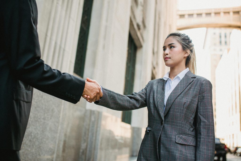 Two business professionals shaking hands outdoors in urban setting, symbolizing partnership.