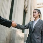 Two business professionals shaking hands outdoors in urban setting, symbolizing partnership.