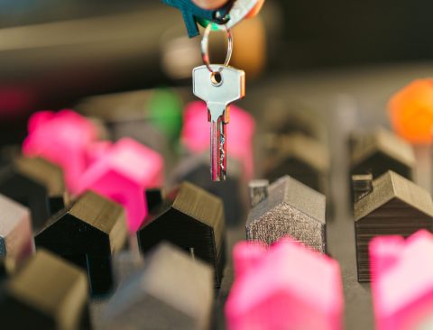 Close-up of a hand holding a key above colorful miniature houses, symbolizing real estate transaction or investment.