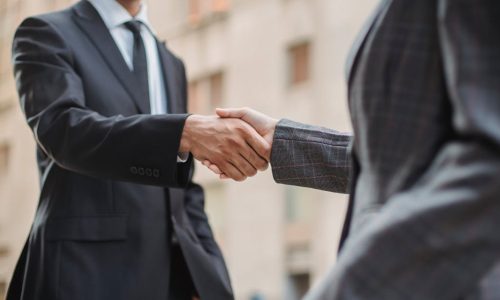 Business professionals greeting each other with a handshake outdoors, symbolizing partnership.