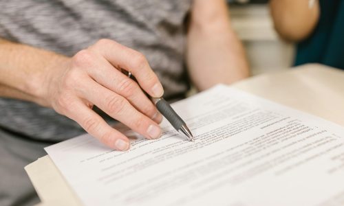 Close-up of a person's hand signing an important legal document with a pen indoors.